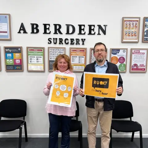 Two Aberdeen Surgery team members holding R U OK? Day posters in the waiting room